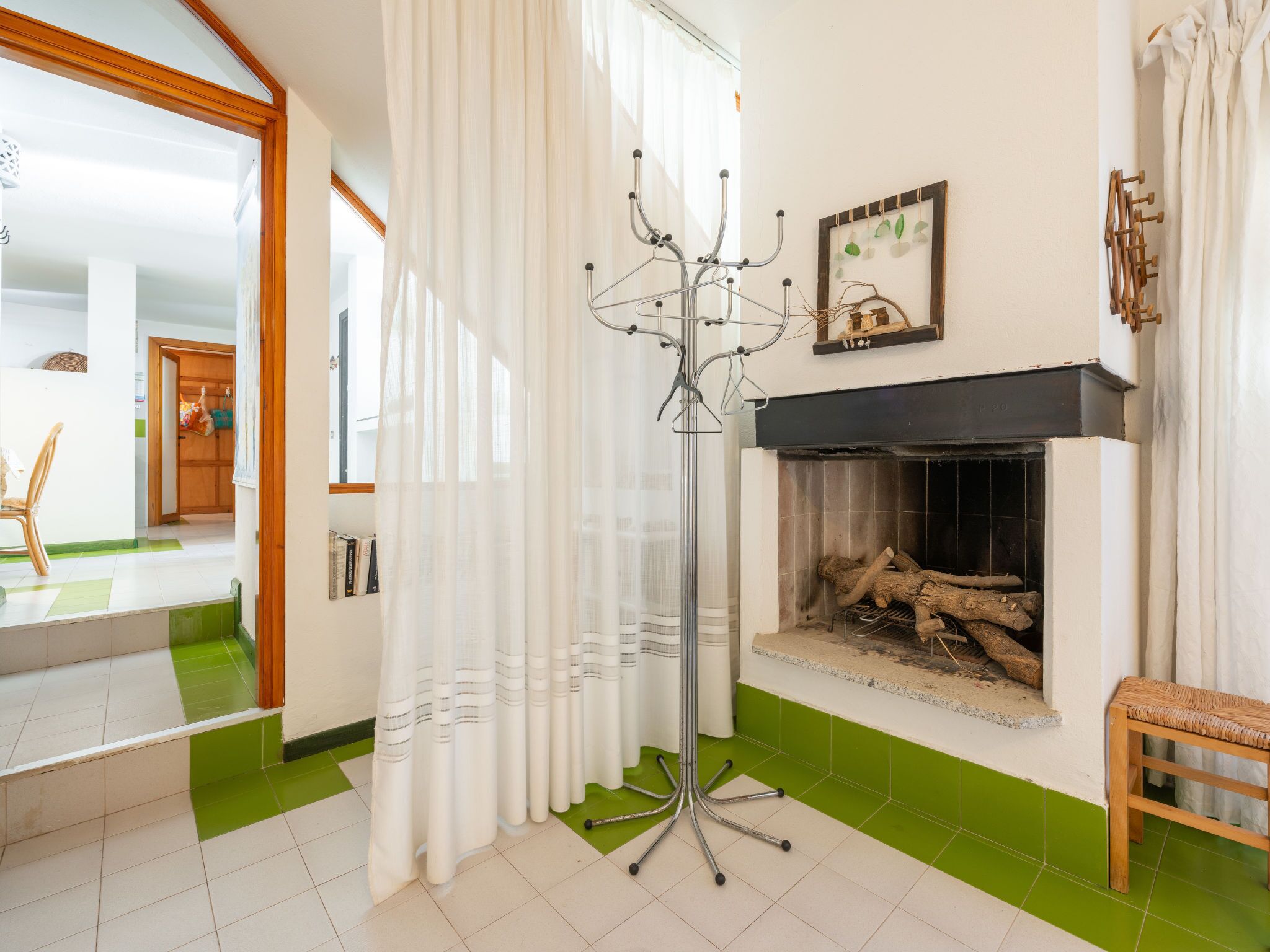 A living room with a fireplace, a coat rack, and a green-tiled floor.