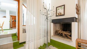 A living room with a fireplace, a coat rack, and a green-tiled floor. - Capo Boi by Interhome (Villasimius)