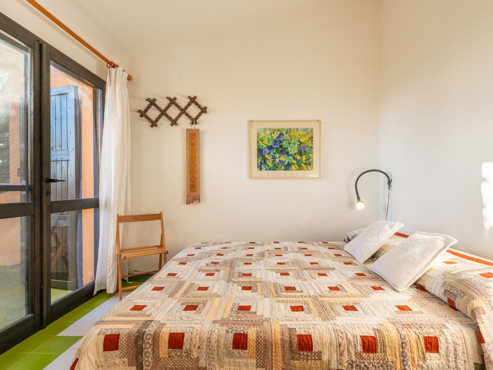 A bedroom with a bed, a chair, a window, a wall-mounted artwork, and a floor lamp.