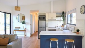 A modern kitchen with white cabinets, stainless steel appliances, and a central island with stools. - Gumleaf - Freycinet Holiday Houses (Coles Bay)