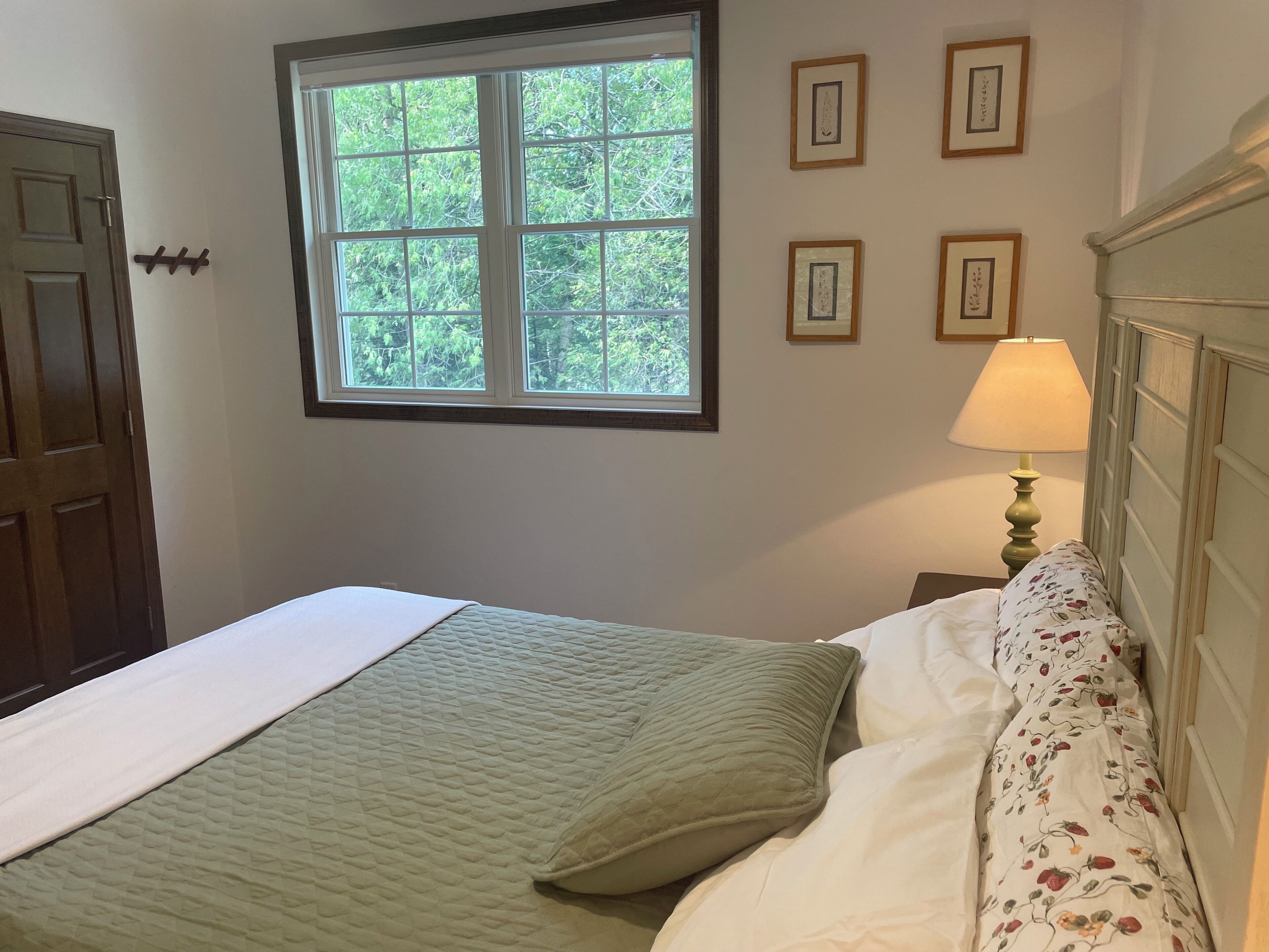 A bedroom with a bed, a window, and a nightstand with a lamp.
