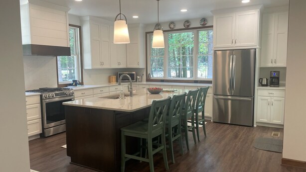 A modern kitchen with white cabinets, stainless steel appliances, a central island with bar stools, and pendant lighting.