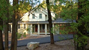A two-story house with a porch, surrounded by trees and a driveway.