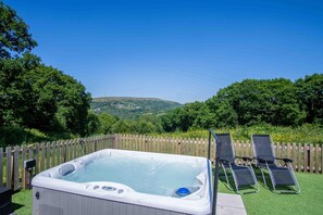 Un jacuzzi con cerca de madera y sillas reclinables en un jardín con vistas a colinas.