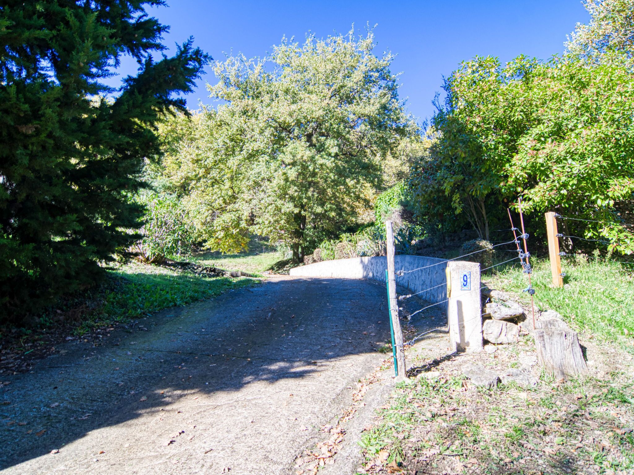 Un chemin pavé traverse une zone boisée et est agrémenté d’une barrière et d’un panneau indicateur.