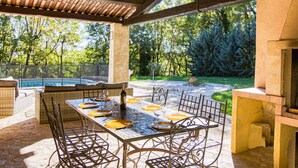 Une terrasse extérieure avec une table dressée pour le repas, entourée de chaises, et une piscine en arrière-plan.