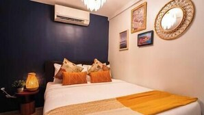 A neatly made bed with a blanket and pillows, an air conditioning unit above it, and a small table with a lamp beside the bed. - Dockyard by Araw Residences (El Nido)