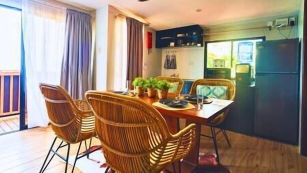 A compact kitchen with a refrigerator, a dining area with wicker chairs, and a ceiling fan. - Dockyard by Araw Residences (El Nido)