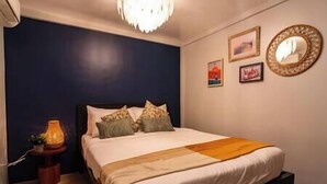 A bedroom with a bed, a bedside table, a lamp, and wall art. - Dockyard by Araw Residences (El Nido)