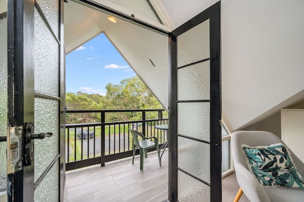 Una habitación con balcón, una silla y vistas al exterior.