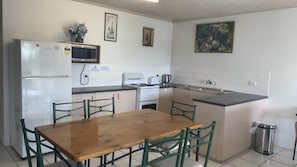 Angolo cottura funzionale con frigorifero, microonde, fornello e lavello. È presente un tavolo con sedie e un cestino.