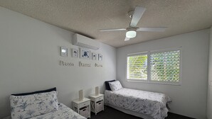 A bedroom with two beds, a ceiling fan, a window with blinds, and wall-mounted air conditioning. - Spinnaker Seas Ocean Views | Walk to Kings Beach | Pool (Kings Beach)