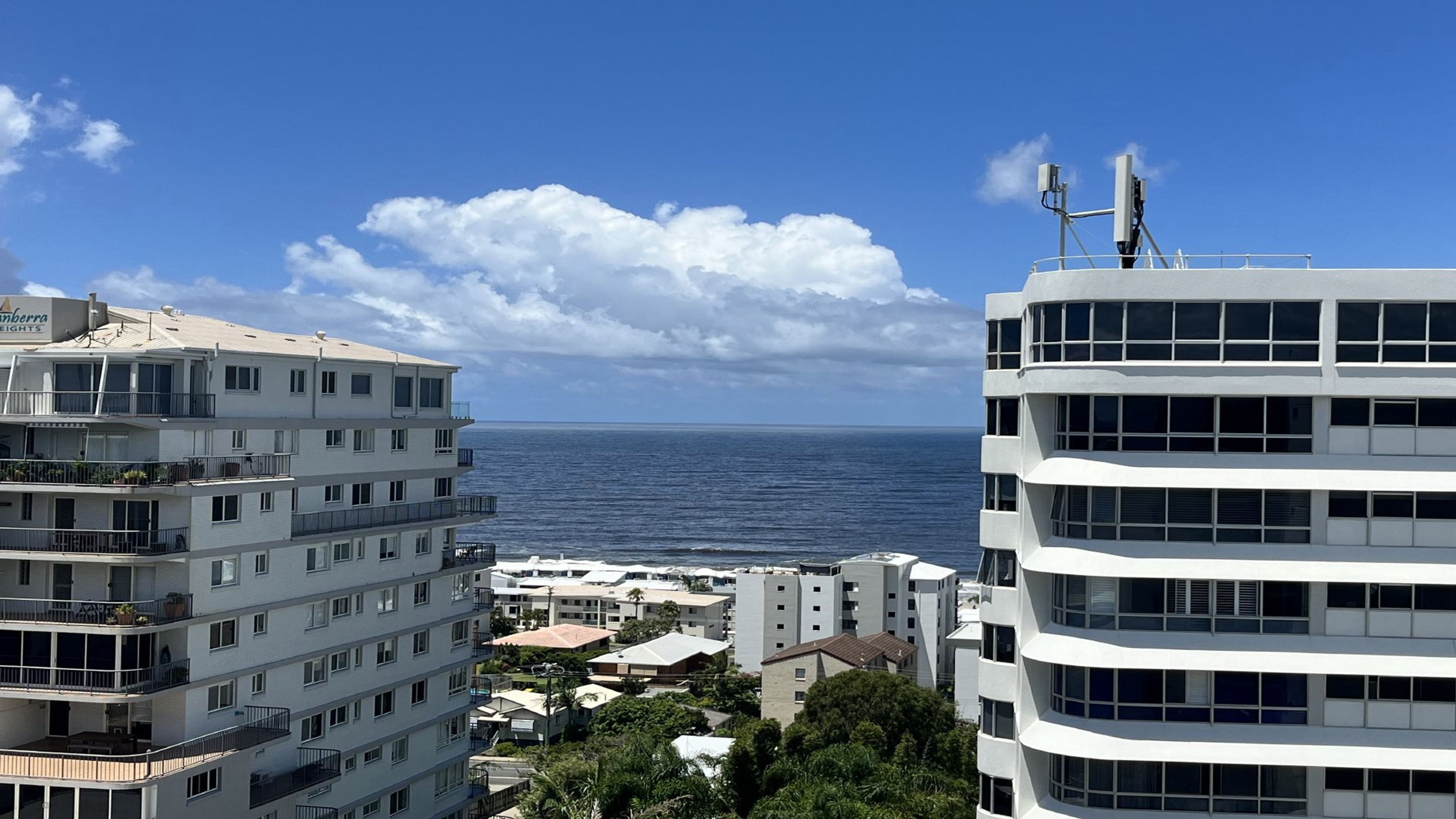 A coastal residential area with multi-story buildings, one with a visible balcony and another with satellite dishes.