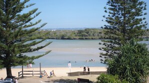 Une plage à l’eau claire, avec un rivage sablonneux, où quelques personnes se baignent.