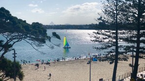 Una playa con un velero, gente y una montaña al fondo.