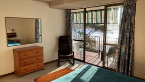 A bedroom with a wooden dresser, a chair, a large mirror, and a view of a balcony with a railing.