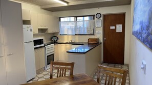 A compact kitchen with a microwave, stove, sink, and a small dining area with two chairs.