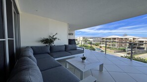 Ein Balkon mit einem grauen Ecksofa, einem kleinen weißen Tisch und einem Blumentopf.