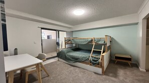 Ein Zimmer mit Etagenbett, Schreibtisch und Stuhl. Eine Schiebetür führt zu einem Balkon.