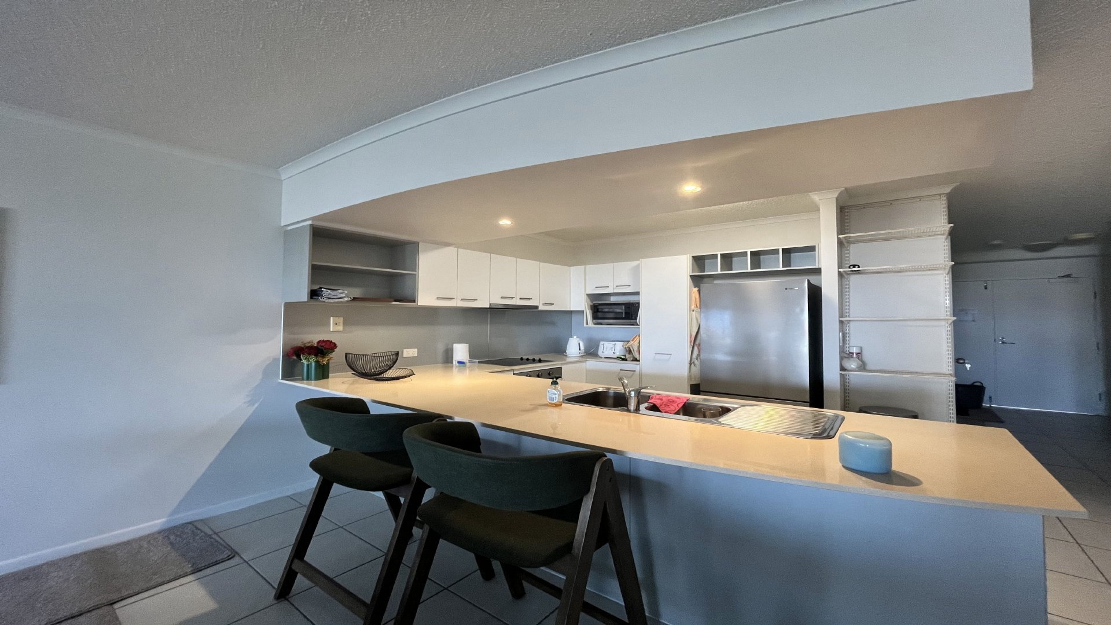 Een moderne keuken met een centraal eiland, barstoelen, een koelkast en een magnetron.
