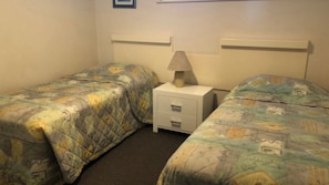 A hotel room with two single beds, a nightstand with a lamp, and a small drawer.