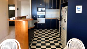 Une cuisine de taille modeste, avec des meubles de couleur sombre, un carrelage à motifs et un petit coin repas agrémenté de chaises en osier.