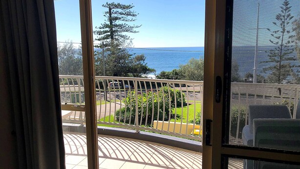Un balcon avec vue sur la mer, un arbre et un sol carrelé.