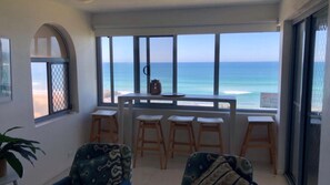A balcony with a view of the ocean, wooden stools, and a table with a kettle.