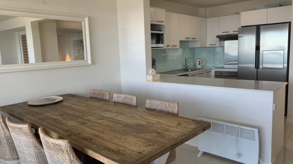 Una cocina moderna con electrodomésticos de acero inoxidable, un comedor con mesa de madera y sillas de mimbre, y un radiador blanco.