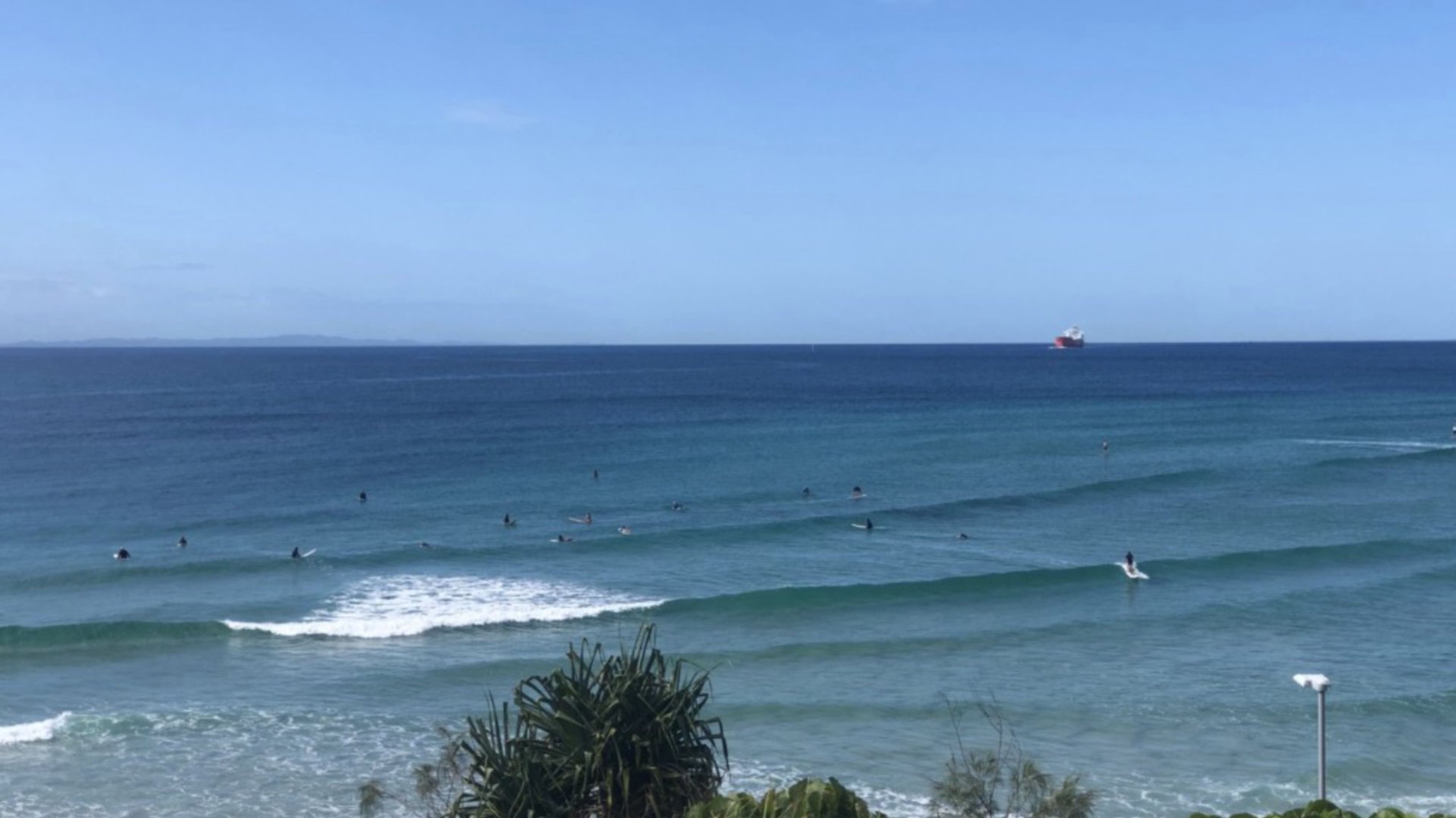 A coastal view with surfers in the water and a ship in the distance.