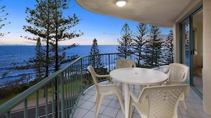 Ein Balkon mit Tisch und Stühlen mit Blick auf die Küste, Bäume und das Meer.