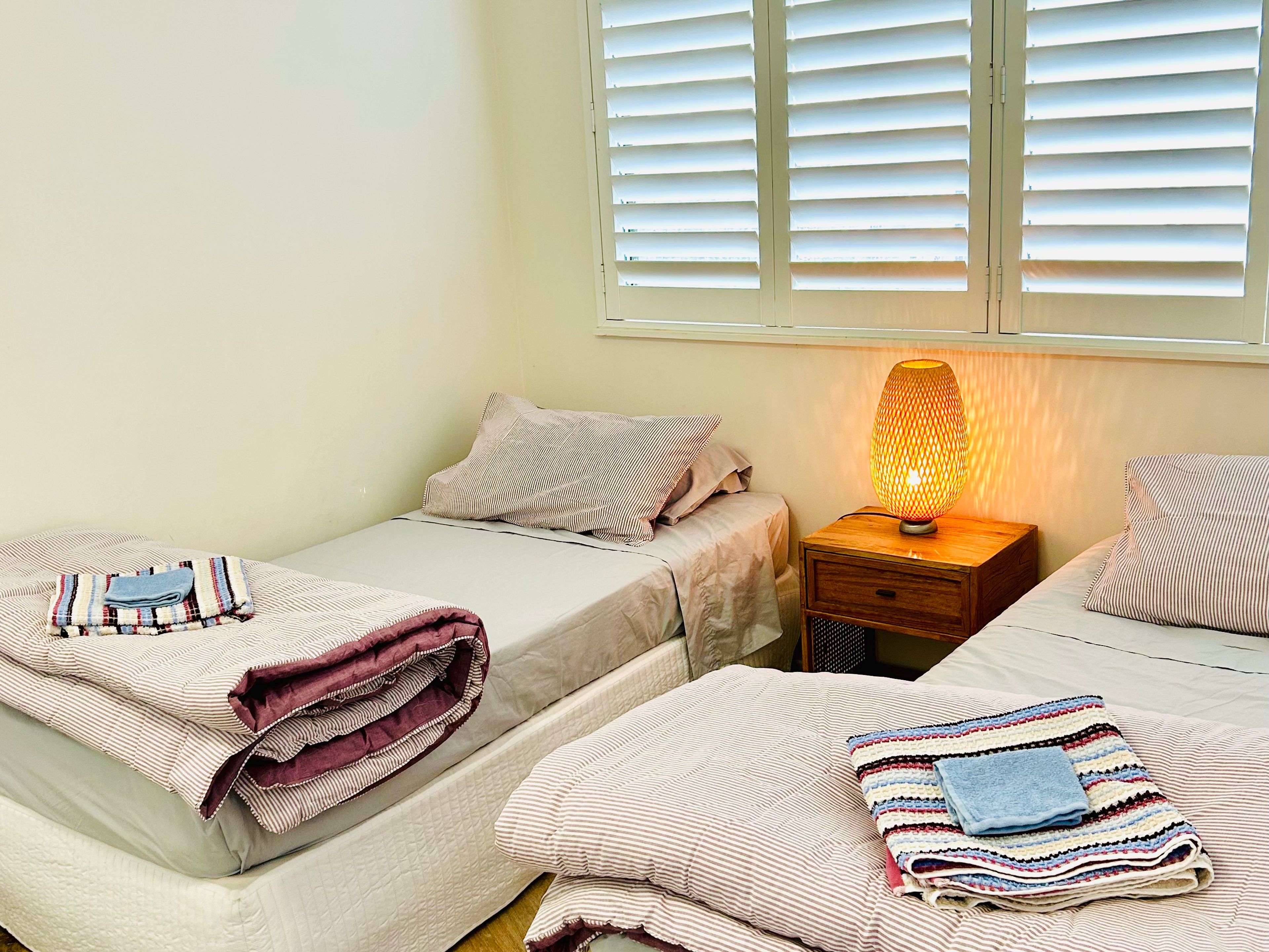 Une chambre avec deux lits, une table de chevet avec une lampe et une fenêtre avec des stores.