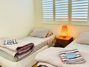 A bedroom with two beds, a nightstand with a lamp, and a window with blinds.