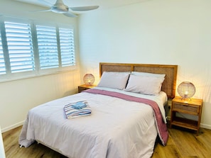 A bedroom with a bed, two bedside tables, a ceiling fan, and a window with blinds.