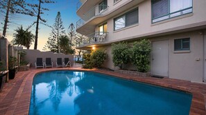Ein Swimmingpool mit Liegestühlen, eine überdachte Terrasse und ein Gebäude mit Balkon.