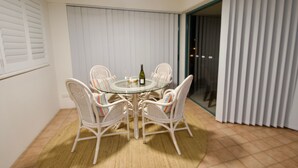 A dining area with a round glass table surrounded by wicker chairs, a bottle of wine, and a glass. - Campbells Cove U12 a Kings Beach Escape (Kings Beach)
