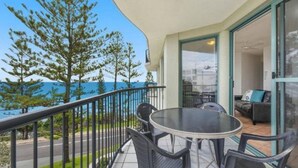 A balcony with a table and chairs, overlooking a body of water and trees. - Campbells Cove U12 a Kings Beach Escape (Kings Beach)