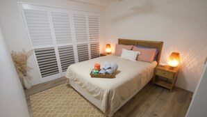 A bedroom with a bed, bedside tables, a nightstand, a window with blinds, and a decorative plant. - Campbells Cove U12 a Kings Beach Escape (Kings Beach)