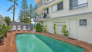 Una piscina con lettini, un edificio con un balcone e alberi sullo sfondo.