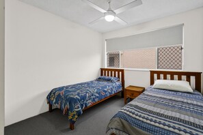 Un dormitorio con dos camas individuales, un ventilador de techo y una ventana con persianas.