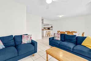 Ein modernes Wohnzimmer mit zwei blauen Sofas, einem Holztisch und einer Küche im Hintergrund.