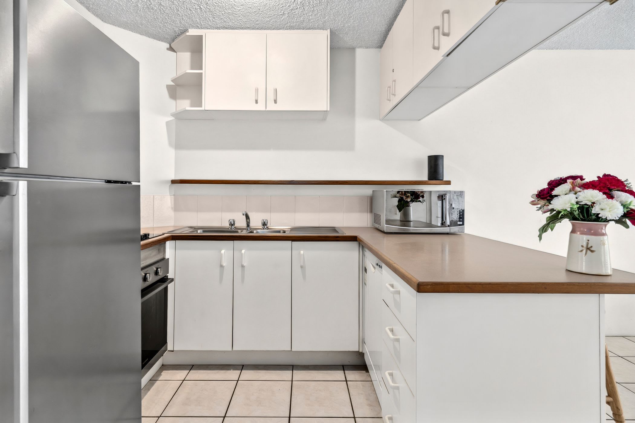 A modern kitchen with white cabinetry, a stainless steel refrigerator, a microwave, and a sink.
