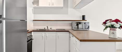 A modern kitchen with white cabinetry, a stainless steel refrigerator, a microwave, and a sink.