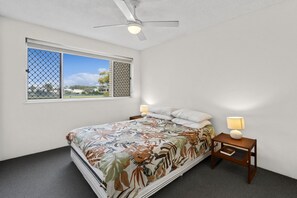 Ein Schlafzimmer mit einem Bett, zwei Nachttischen, einem Deckenventilator und einem Fenster mit Blick.