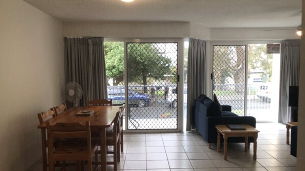 A room with a dining table, chairs, a sofa, a TV, and a sliding glass door leading to an outdoor area.