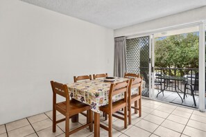 A dining area with a table and chairs, a patterned tablecloth, and a view of the outdoors through a sliding glass door.