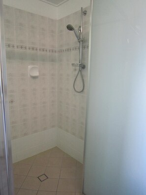 Ein kleiner, abgeschlossener Duschbereich mit Handbrause und am Wand befestigtem Wasserhahn.
