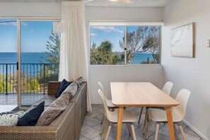 A room with a balcony, a dining table with chairs, a sofa with cushions, and a view of the sea. - Shoreline U2 Walk To Kings Beach & Parklands (Kings Beach)
