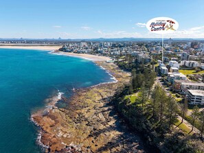 A coastal cityscape with a beach, residential buildings, and a prominent sign for Caloundra Holiday Centre. - Shoreline U2 Walk To Kings Beach & Parklands (Kings Beach)