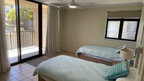 Habitación con dos camas, ventilador de techo, ventana con persianas y vista al exterior.
